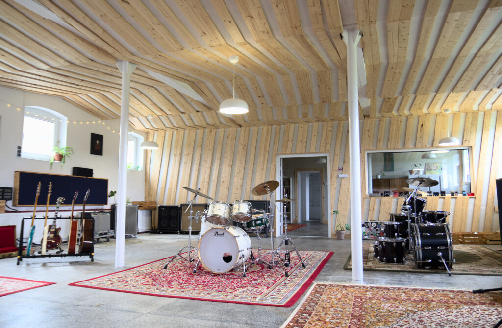 Spacious live room with instruments; it's full of light from both the outside and ceiling lights. Rugs on the floor make the room look cosy.